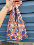 Mini reusable tote bag. Orange bag with multi-color floral print. Print by Dave Hill.